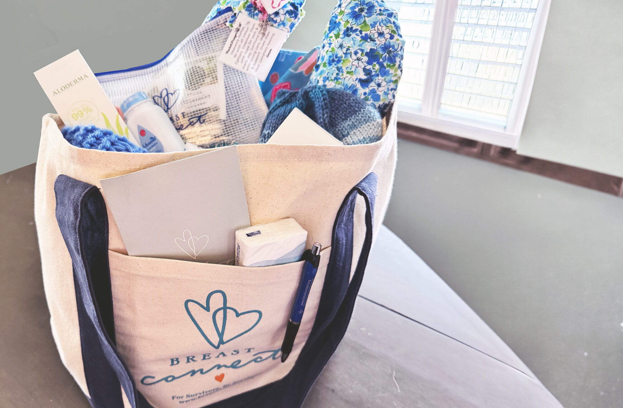 Breast Connect Heart-to-Heart Care Package &mdash; logo tote bag filled with comfort items, handmade knit cap, lotion, journal, and pen